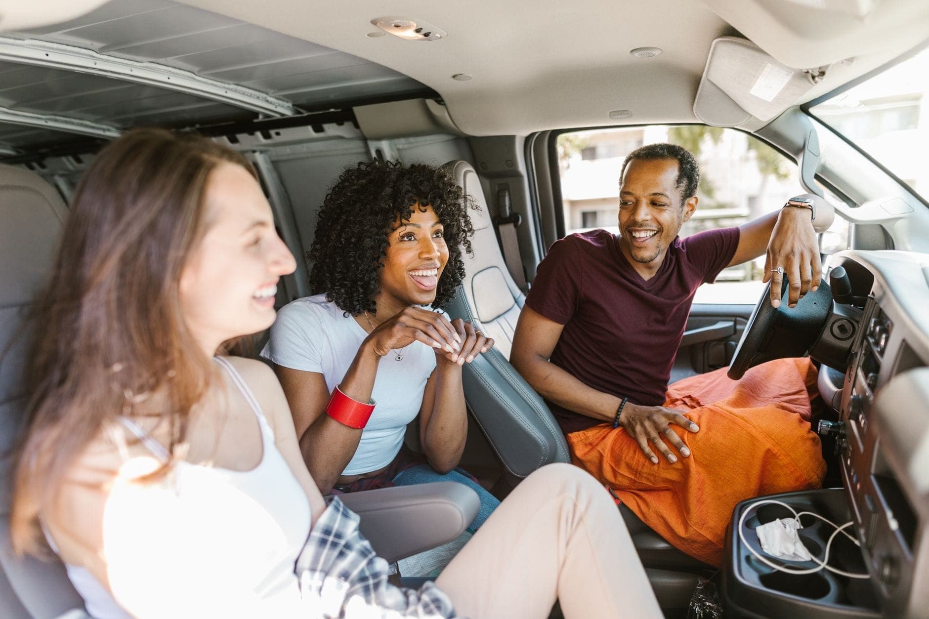 A group of friends laughing inside a passenger van, travelling together in one maxi cab instead of splitting across several cars